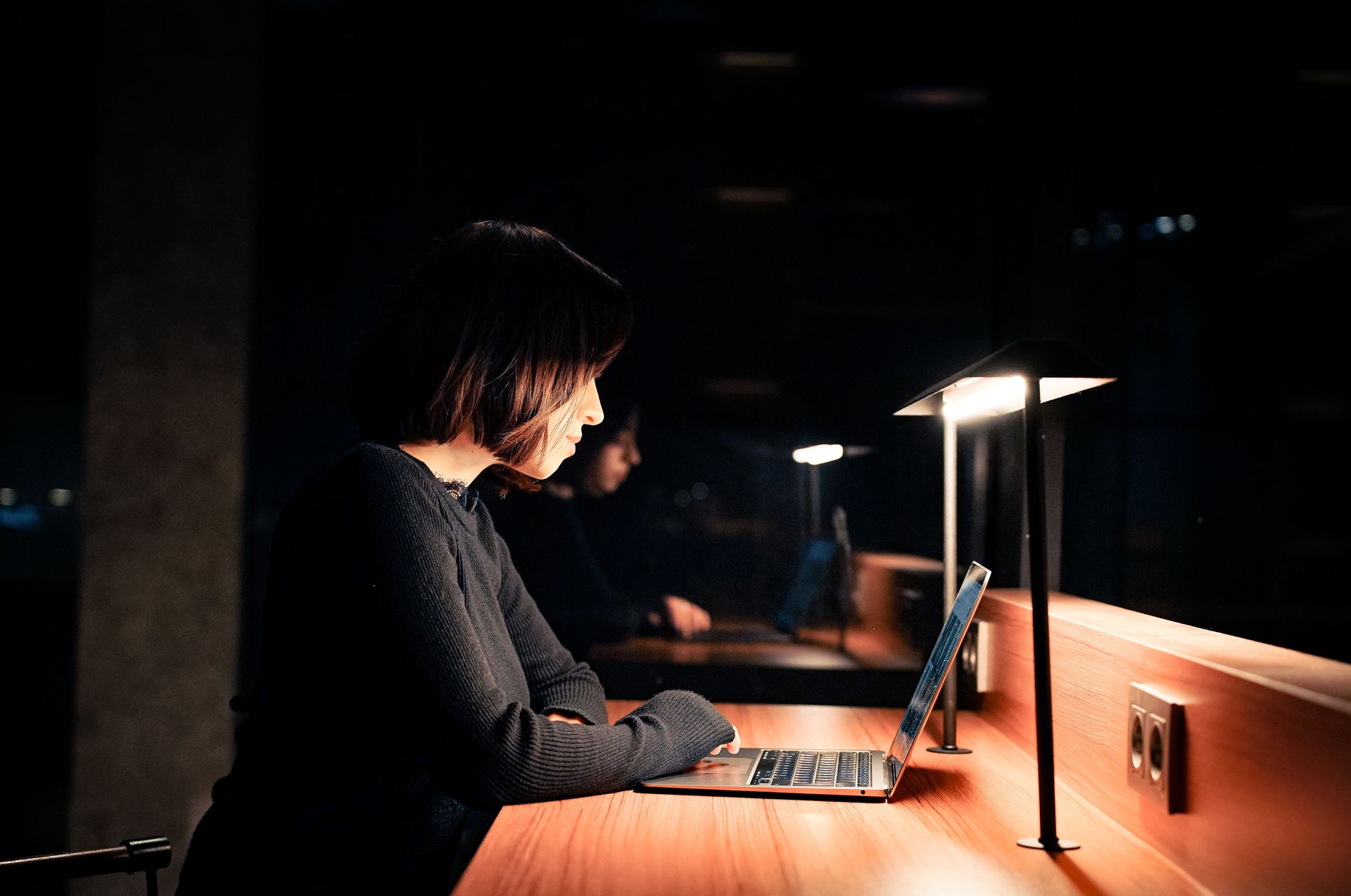 A builder working at a laptop late at night, one warm light in a dark room