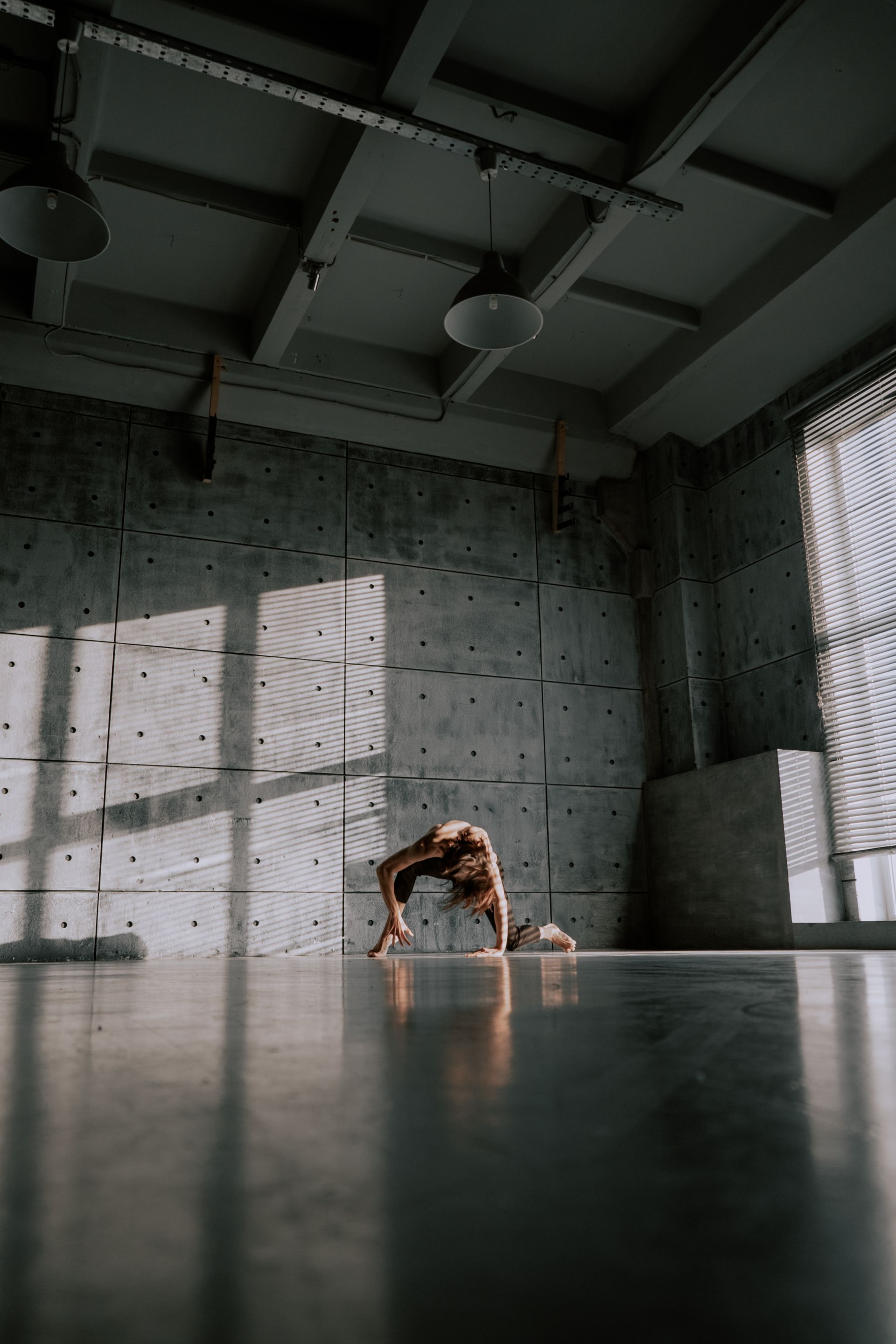 A dancer practicing contemporary movement alone in an industrial studio, hard light cutting shadows