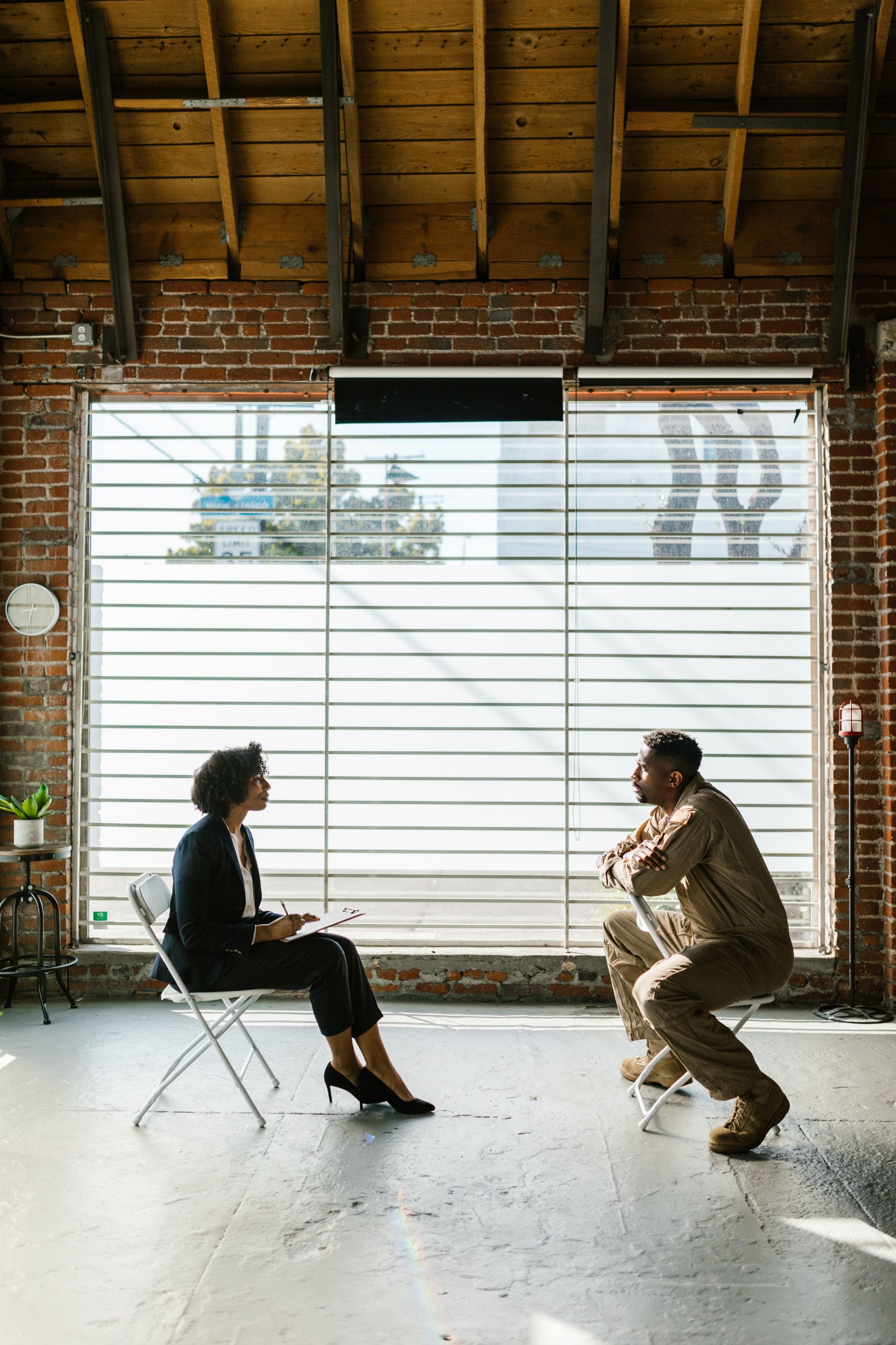 Two people in a quiet one-on-one conversation beside a window, one taking notes